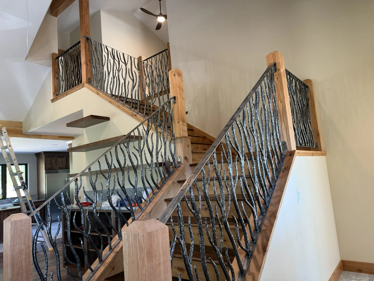 Branch-like forged steel railing installed beside wood stairs and around the upper landing