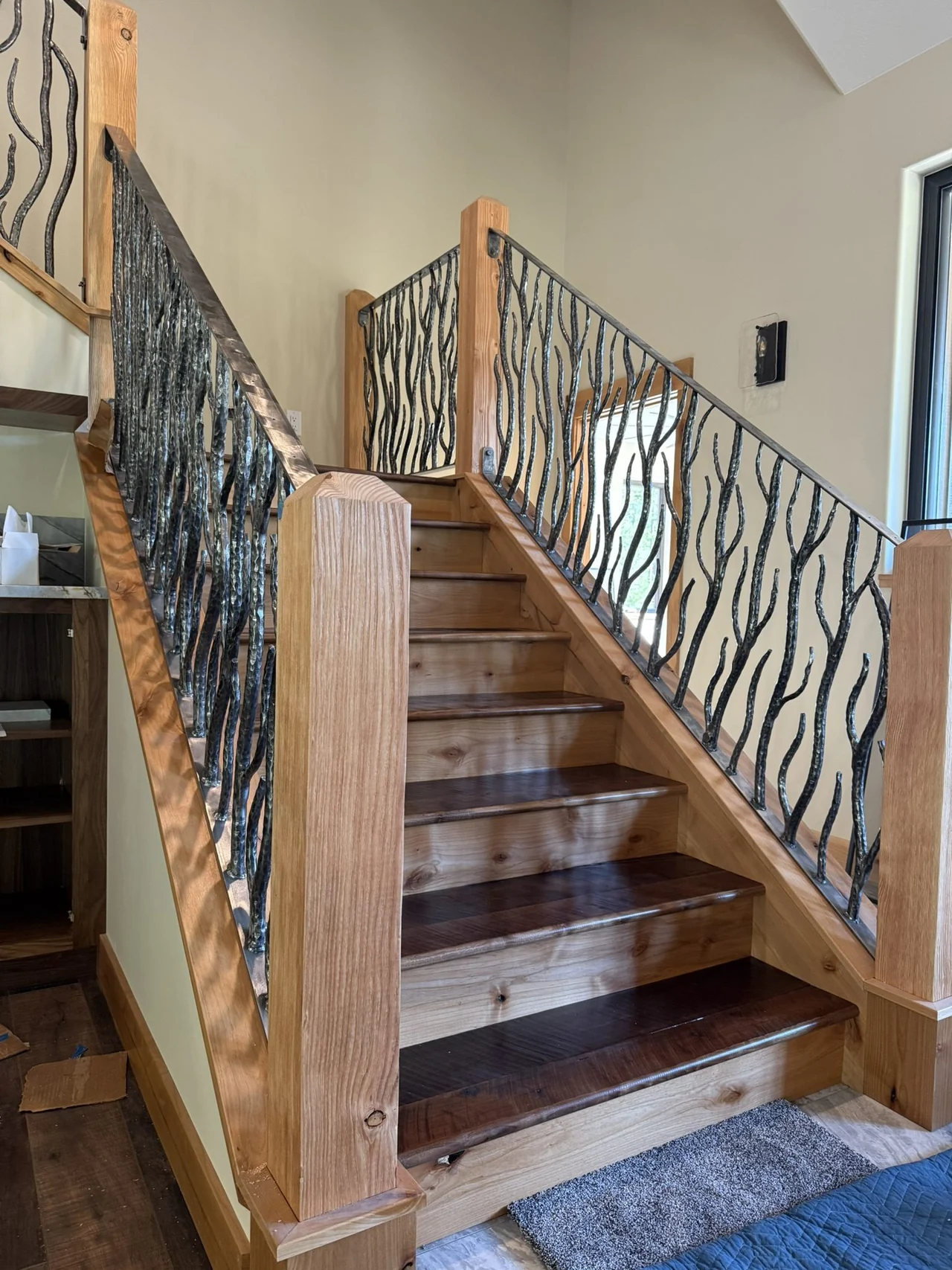 Finished hand-forged stair railing installed beside a wood staircase